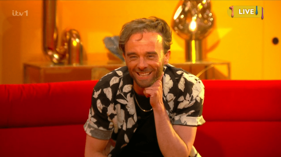 Smiling man on a red sofa during a live television show.