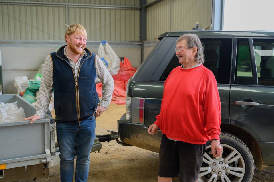 Two men stand in a barn, one leaning on a trailer.  Jeremy Clarkson's Farm series 4.