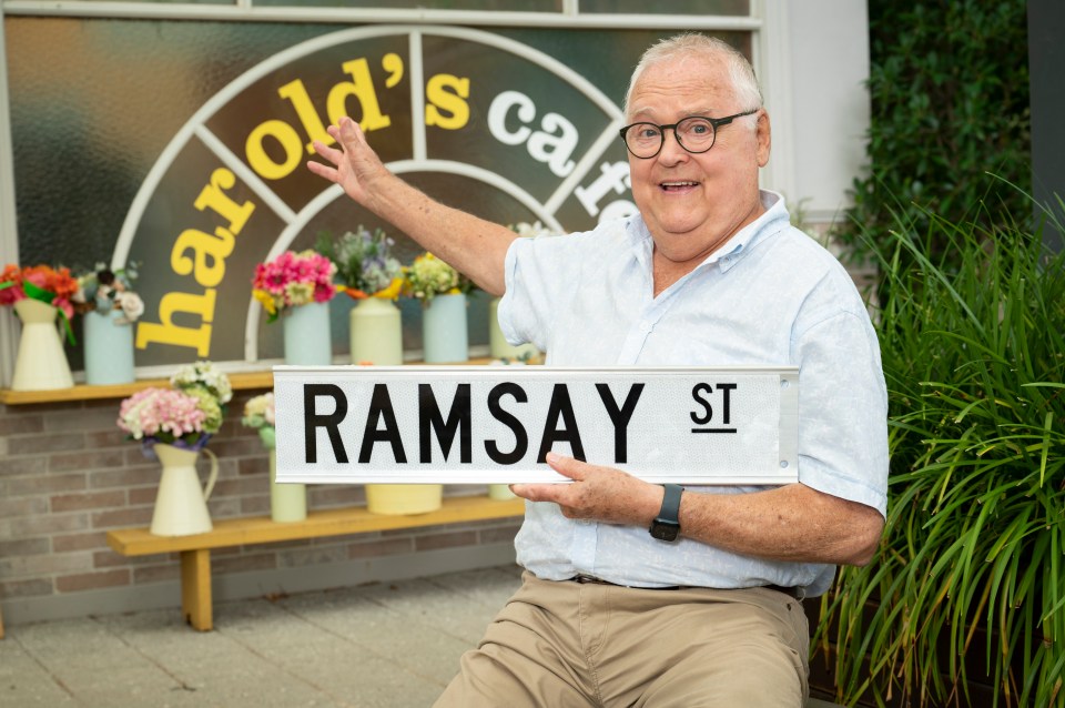 Ian Smith holding a Ramsay Street sign.