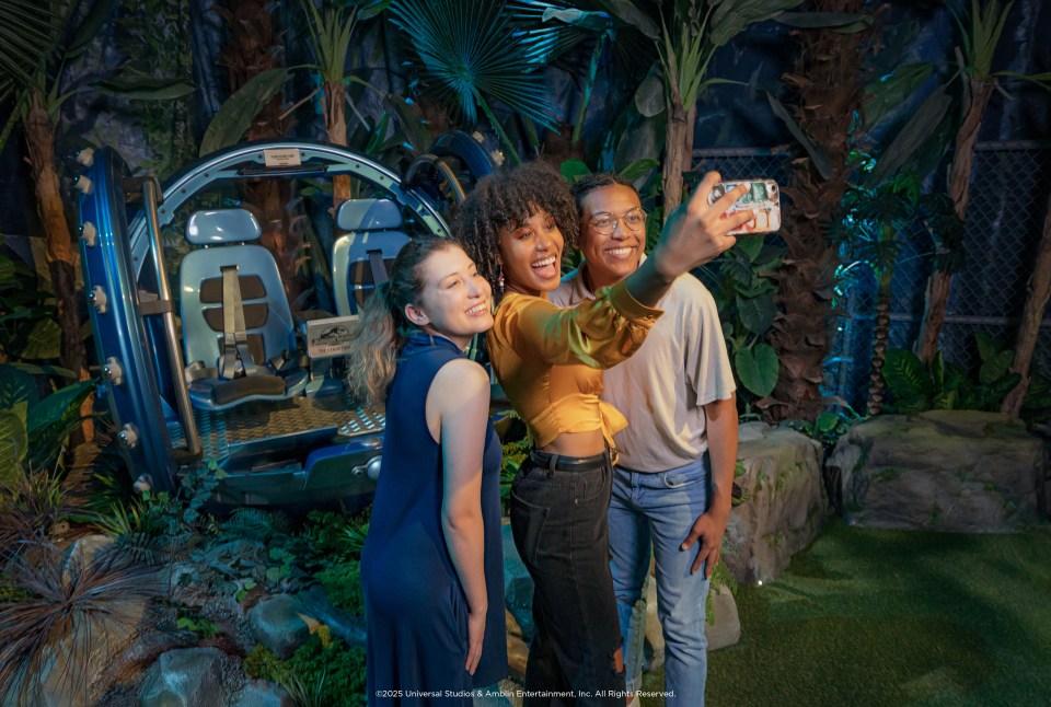 Three people taking a selfie in front of a Jurassic World ride.