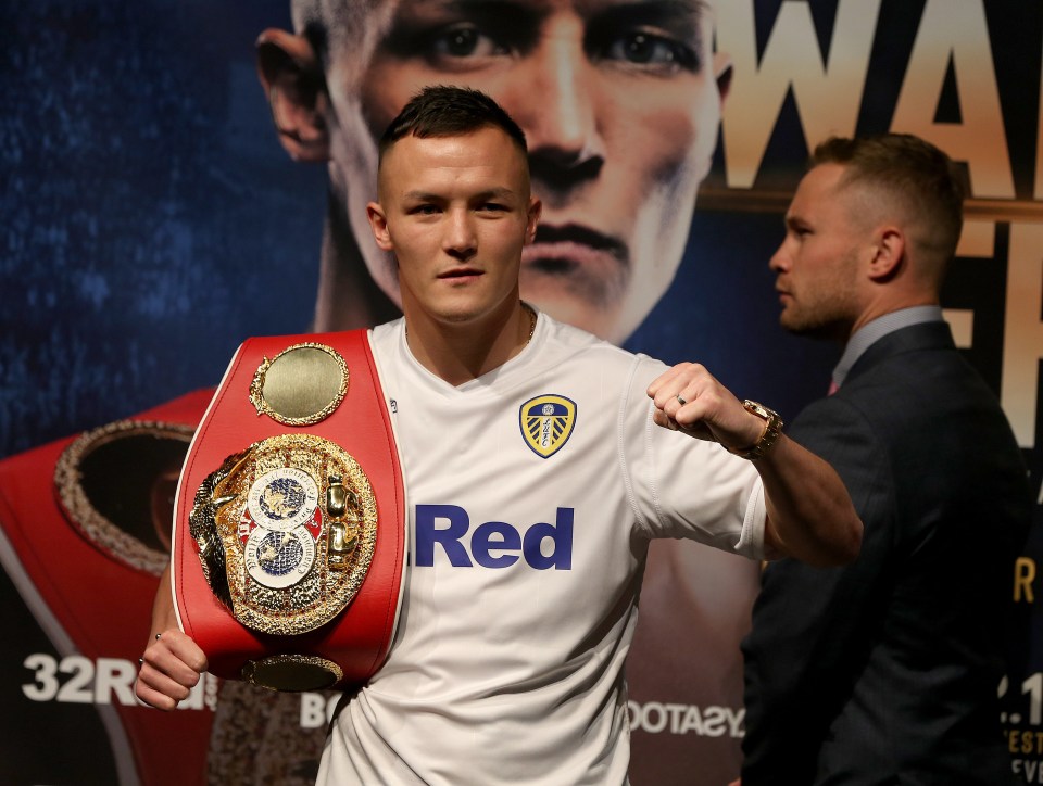 Josh Warrington holding a boxing championship belt at a press conference.
