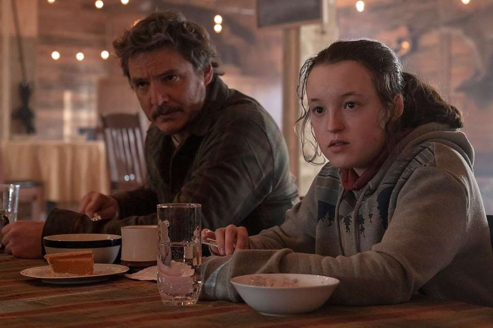 Still from The Last of Us season 2 showing a man and a young woman sitting at a table.
