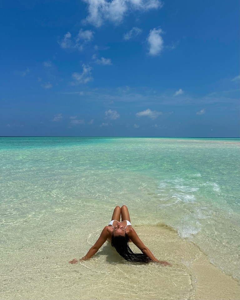 Woman in white bikini relaxing in shallow, clear ocean water.