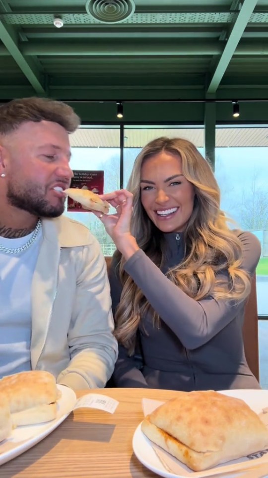 A woman feeds a man a sandwich.
