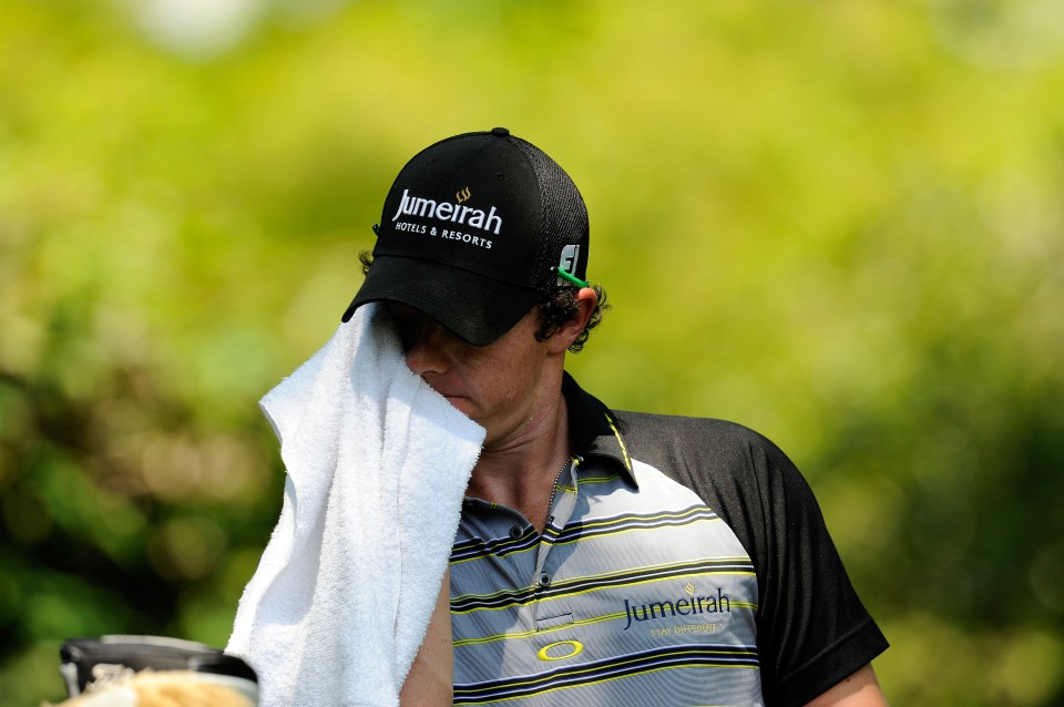 Rory McIlroy wiping his face with a towel during a golf tournament.