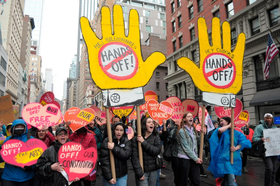 Protestors march in Manhattan holding signs that say "Hands Off!" and address billionaires, crooks, and various social issues.