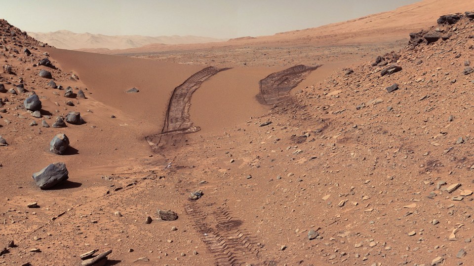 Mars rover tire tracks in a rocky, sandy landscape.