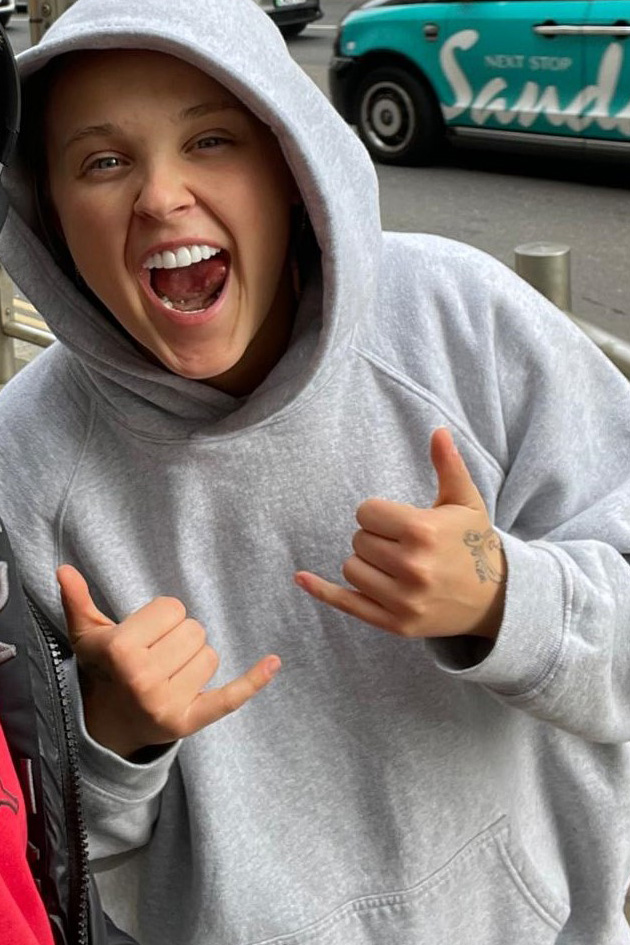 Woman in gray hoodie making shaka sign.
