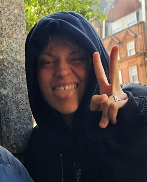 Close-up of a person wearing a dark hoodie, making a peace sign.