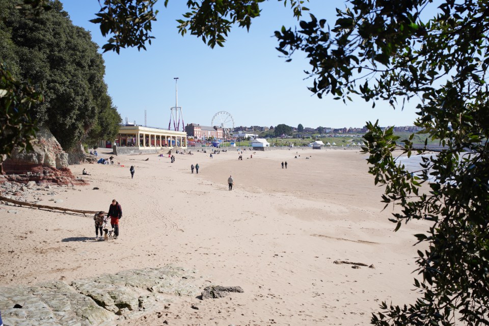 People enjoying a sunny day at a beach with a Ferris wheel and amusement park rides in the background.