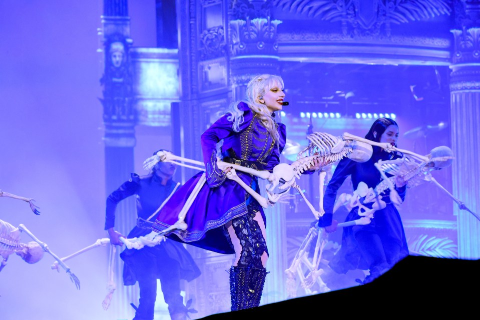 Lady Gaga performing on stage with dancers and skeletons.
