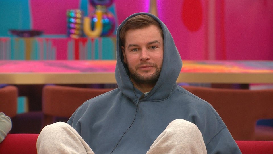 A man wearing a gray hoodie sits in a brightly colored room.