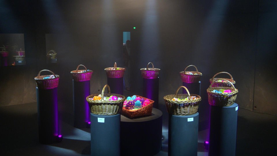Baskets of colorful eggs on pedestals in a dark room.
