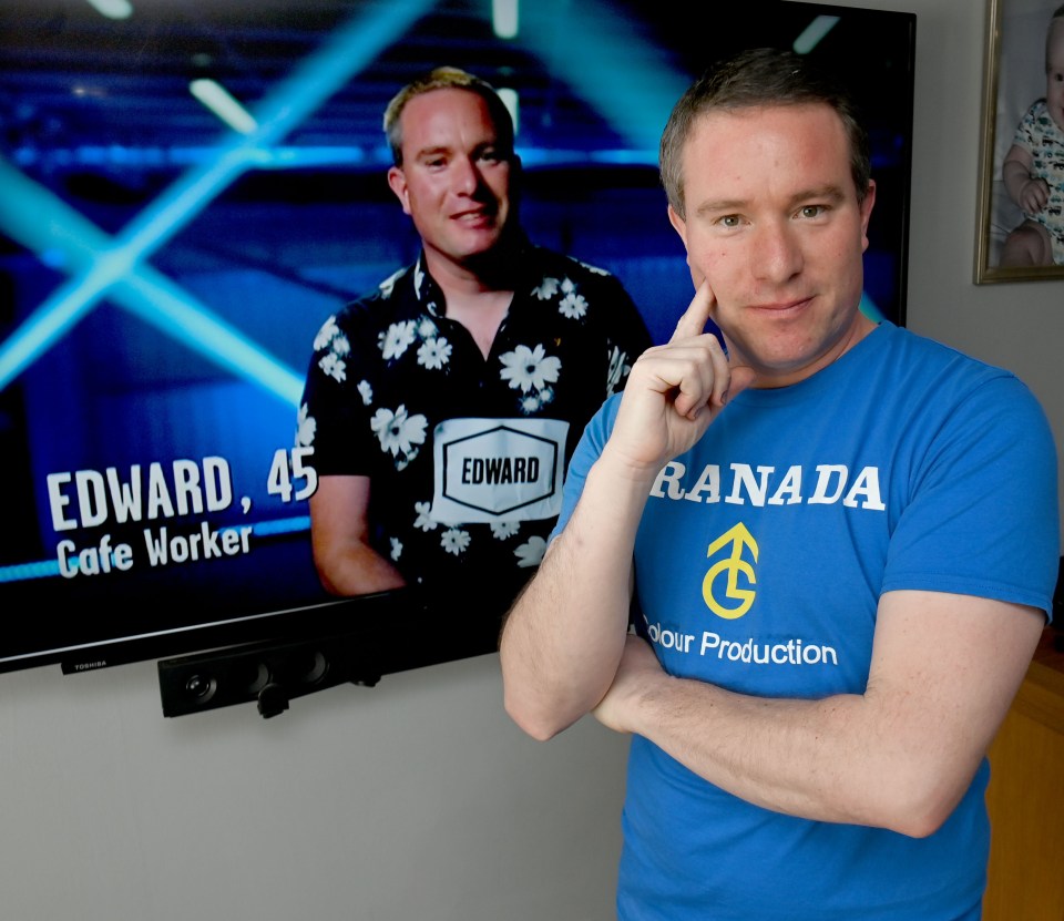 A man in a blue shirt stands in front of a TV showing him on a game show.