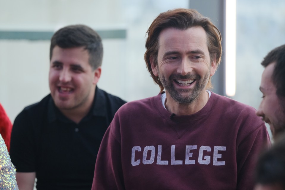 David Tennant smiling in a maroon sweatshirt that says "COLLEGE".