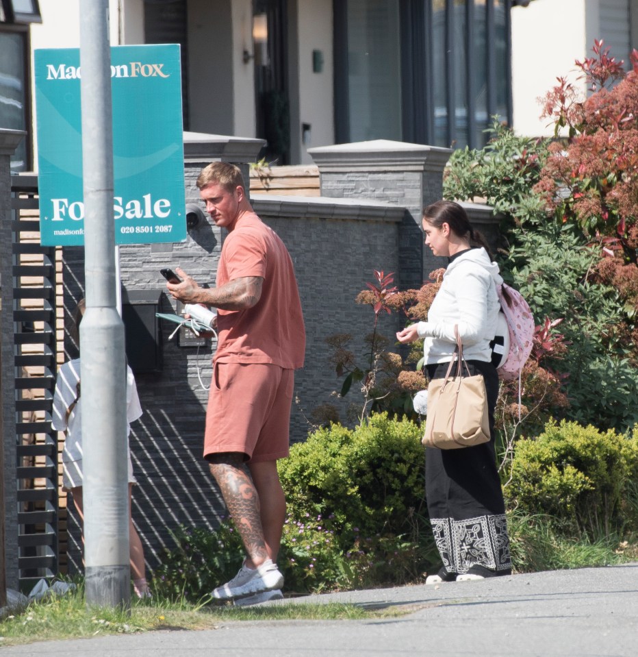 A man and woman stand outside a home; the man is looking at his phone.