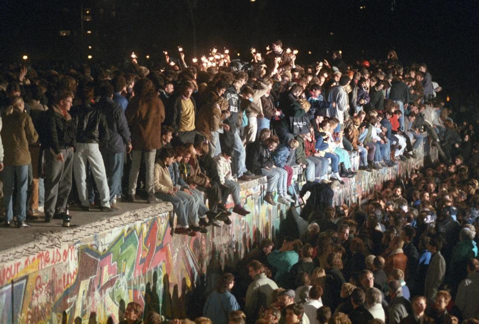 People celebrating on the Berlin Wall with sparklers.
