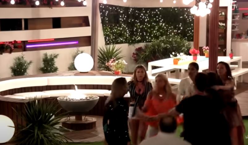 Group of people interacting in a Love Island villa at night.