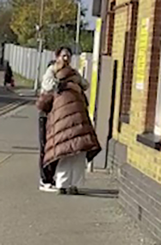 Two people embracing on a sidewalk.