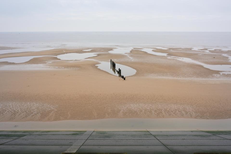 Low tide on Anchorsholme beach in Lancashire, UK, showing a sandy beach with pools of water and a line of old wooden posts.