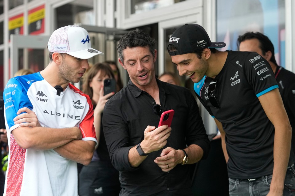 Rory McIlroy showing a photo on his phone to two Alpine Formula One drivers.