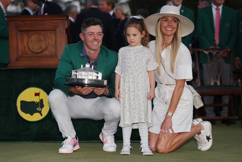 Rory McIlroy with his daughter and wife holding the Masters trophy.