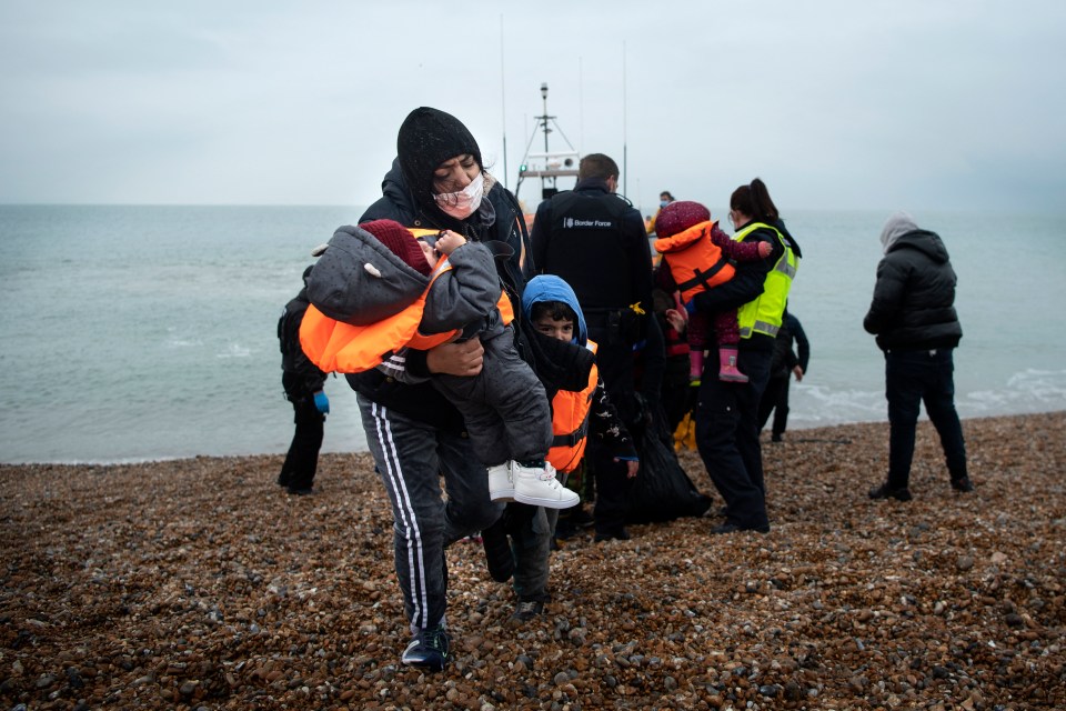 Migrant family arriving on a beach after a Channel crossing, children wearing life vests.