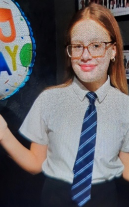 Girl in school uniform holding a birthday balloon.