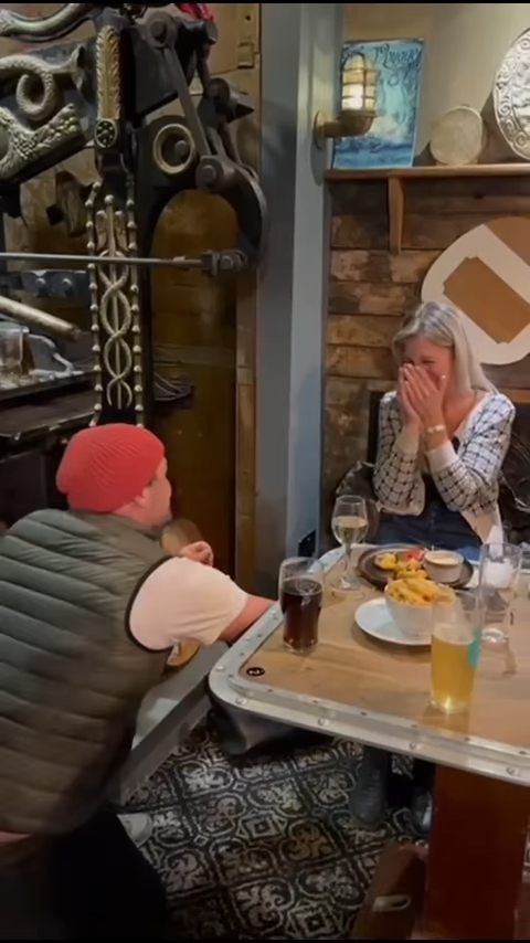 A man proposing to a surprised woman at a restaurant.