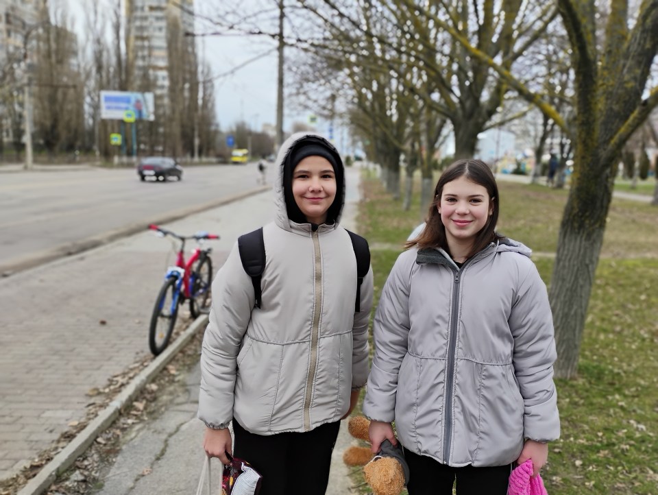 Two Ukrainian girls on a sidewalk, holding stuffed animals.