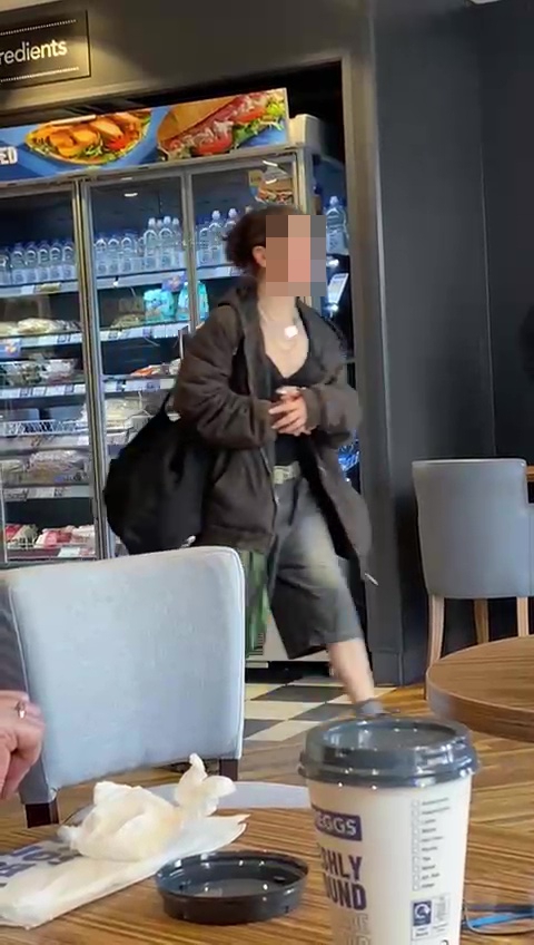 Woman with dreadlocks leaving a Greggs store with food.