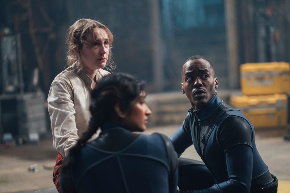Three people looking in different directions in a Doctor Who scene.