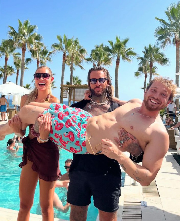 Three people by a pool; one person is being held up by another.