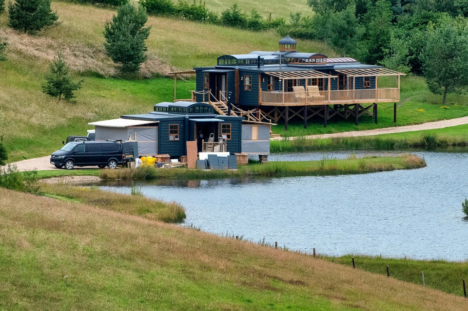 Photo of two dark-colored cabins near a pond, with a van parked nearby.