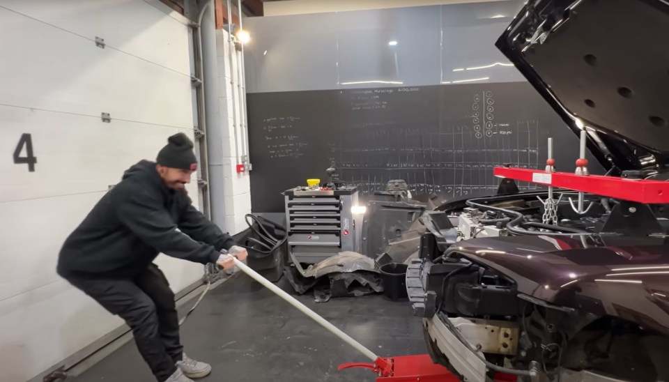 Man moving a damaged Rolls-Royce with a lever in a repair shop.