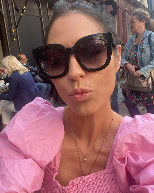 Woman in pink puff-sleeve top and sunglasses making a kissy face.