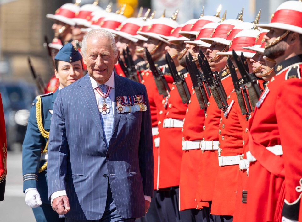 King Charles III in Canada, walking past a line of guards in red uniforms.