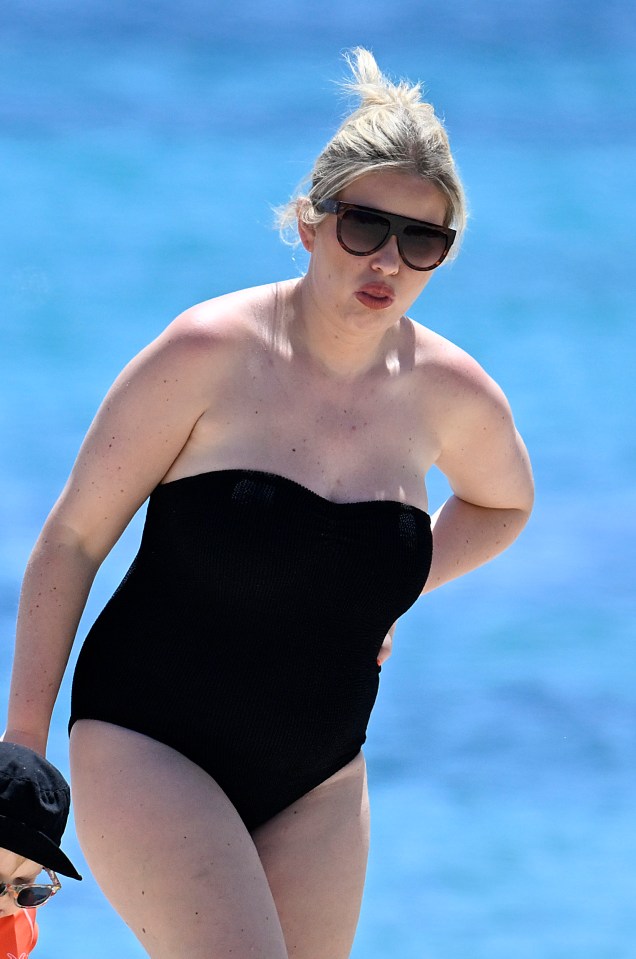 Amy Hart at the beach in a black swimsuit.