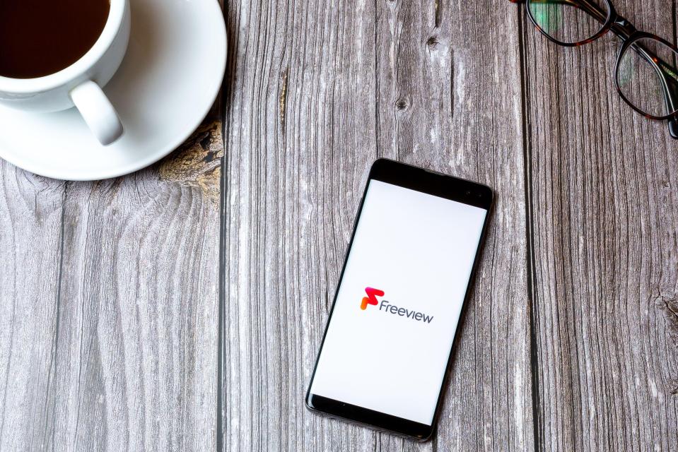 Smartphone displaying the Freeview app on a wooden table next to a cup of coffee and glasses.