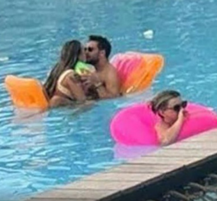 Couple kissing in a pool with another person in a pink floatie.
