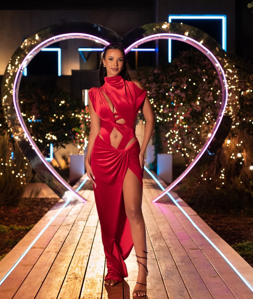 Maya Jama in a red dress standing in a heart-shaped archway.