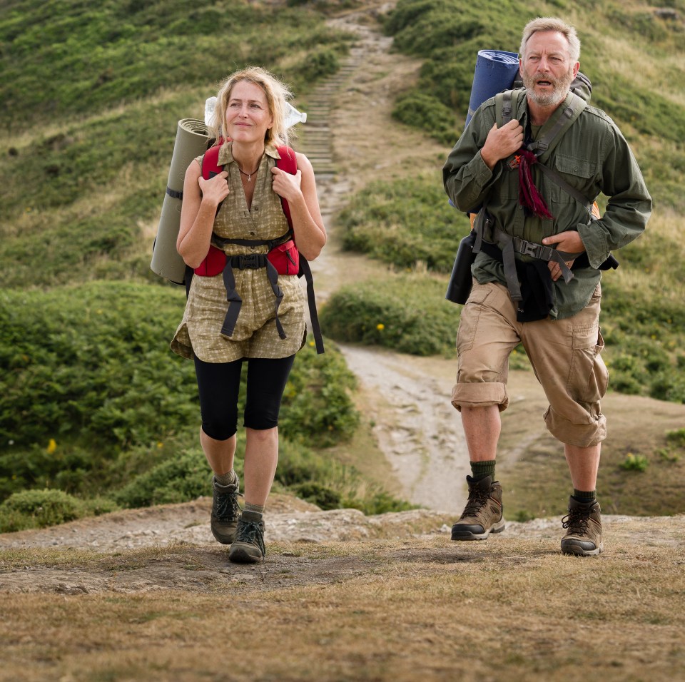 Two hikers with backpacks walking on a path towards a stone structure on a hill.