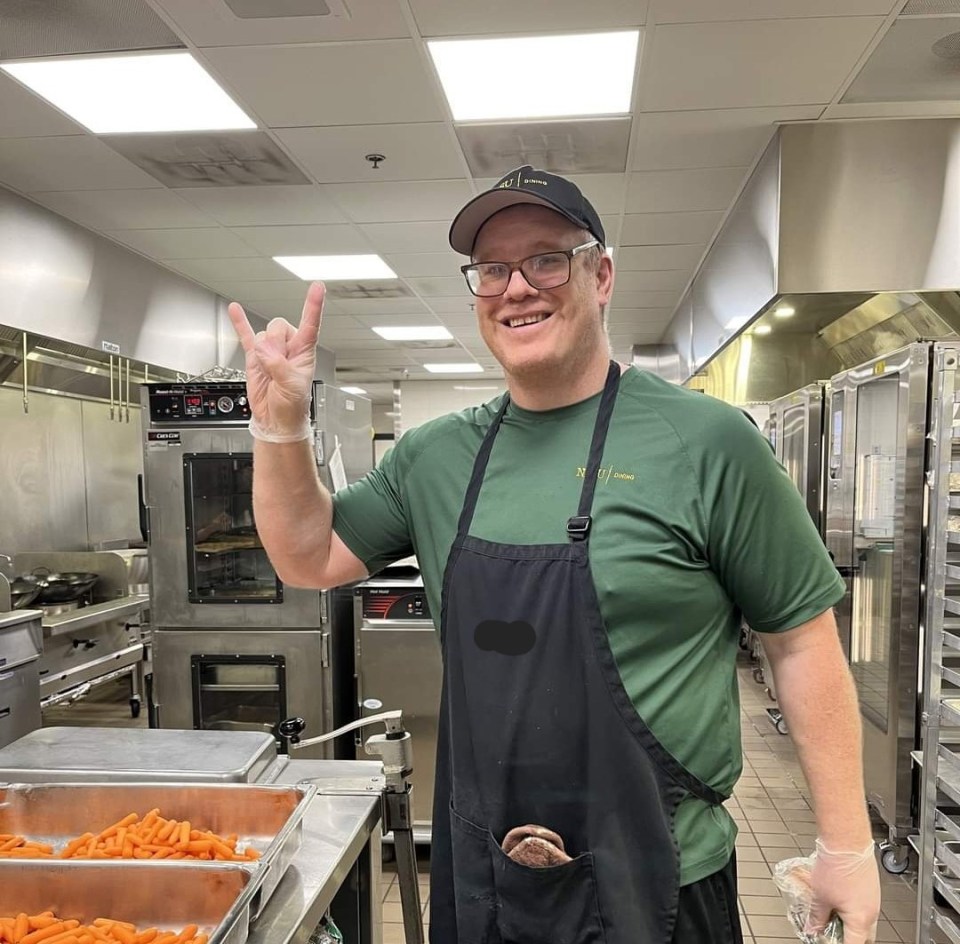 Man in a restaurant kitchen giving a rock-on hand gesture.
