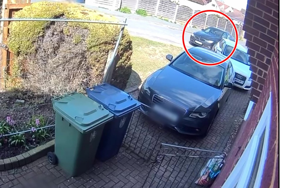 Security camera footage of a dark-colored car driving down a residential street.