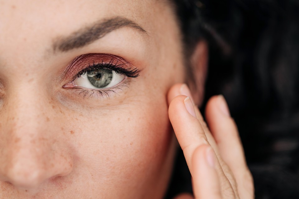 Close-up of a woman's face, highlighting her gray eyes, freckles, and rosy makeup.