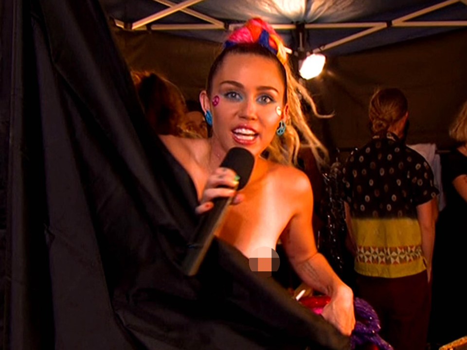 Miley Cyrus topless, holding a microphone.