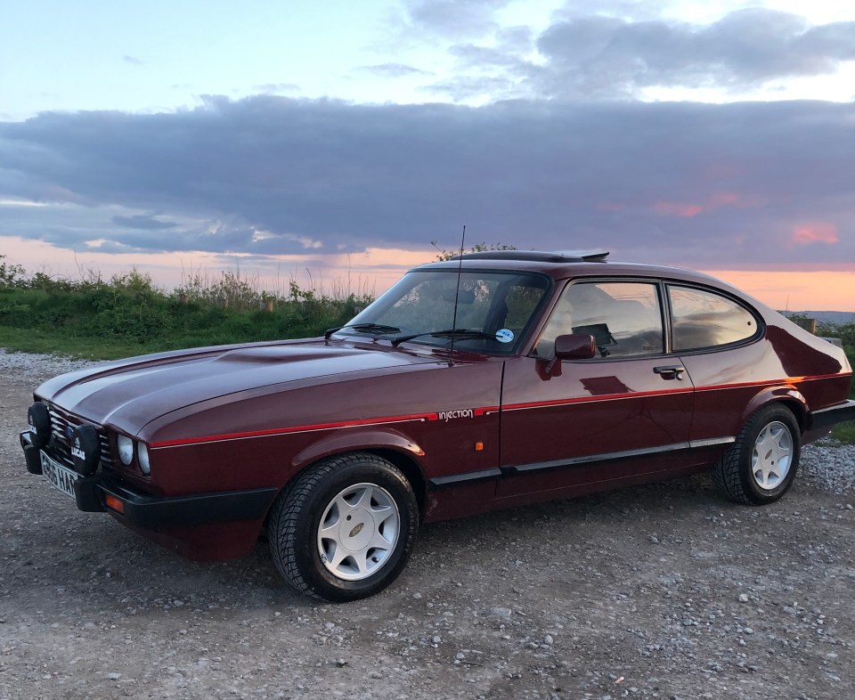 Maroon Ford Capri parked outdoors at sunset.