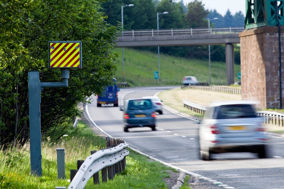 Cars driving past a speed camera on a UK road.