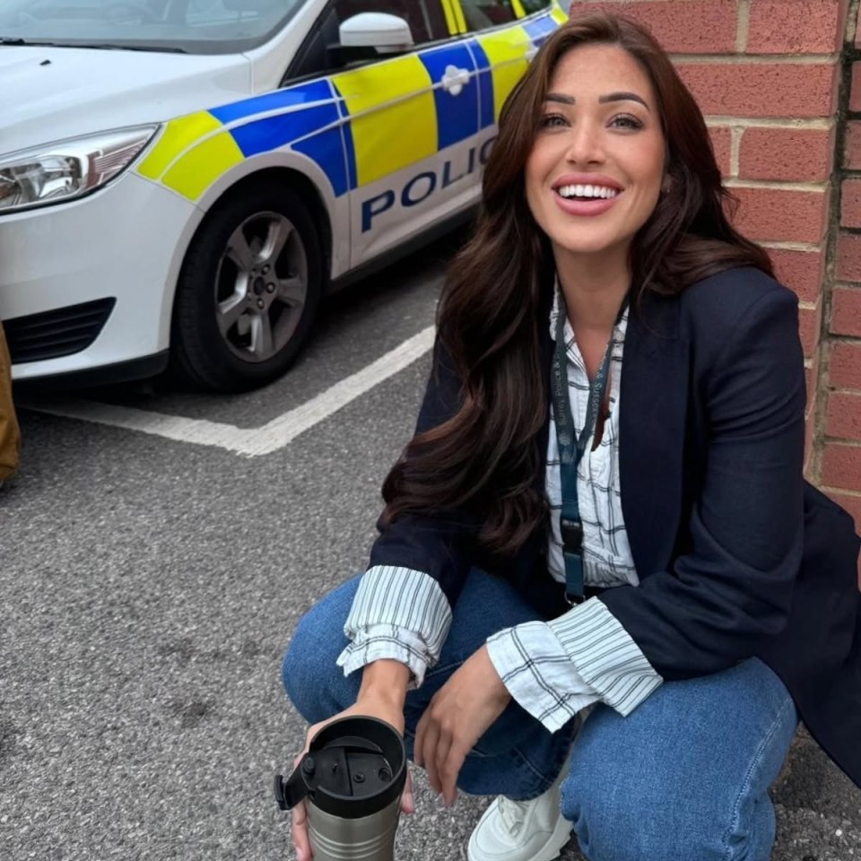 Woman crouching beside a police car, holding a travel mug.
