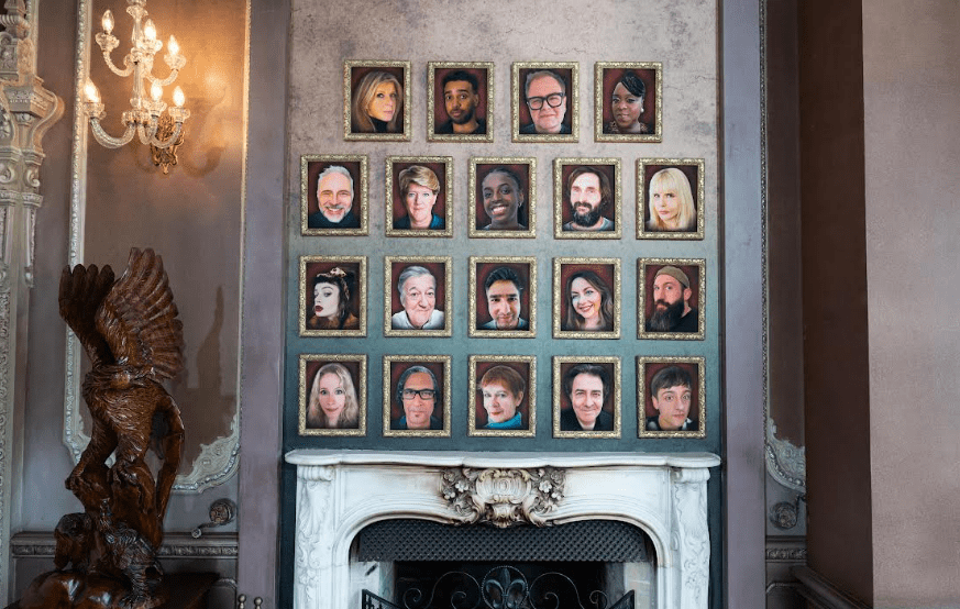 Wall with framed portraits of various people above a fireplace.